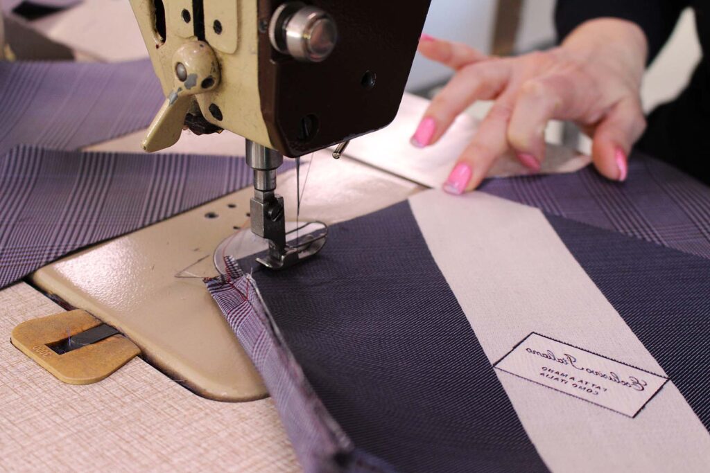 una sarta unisce i pezzi della cravatta utilizzando una macchina da cucire